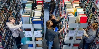 Studierende suchen nach Büchern in der Bibliothek Studierende stehen suchend an mehreren Bücherregalen in der Bibliothek.
